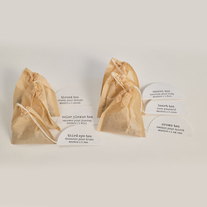  Six bags with their name tags from the Chakra Tea Collection on a white background, including Throat Tea, Solar Plexus Tea, Third Eye Tea, Sacral Tea, Heart Tea, and Crown Tea 