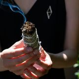 A woman holding a palo santo in her hand wearing a t-shirt with ALTYR logo